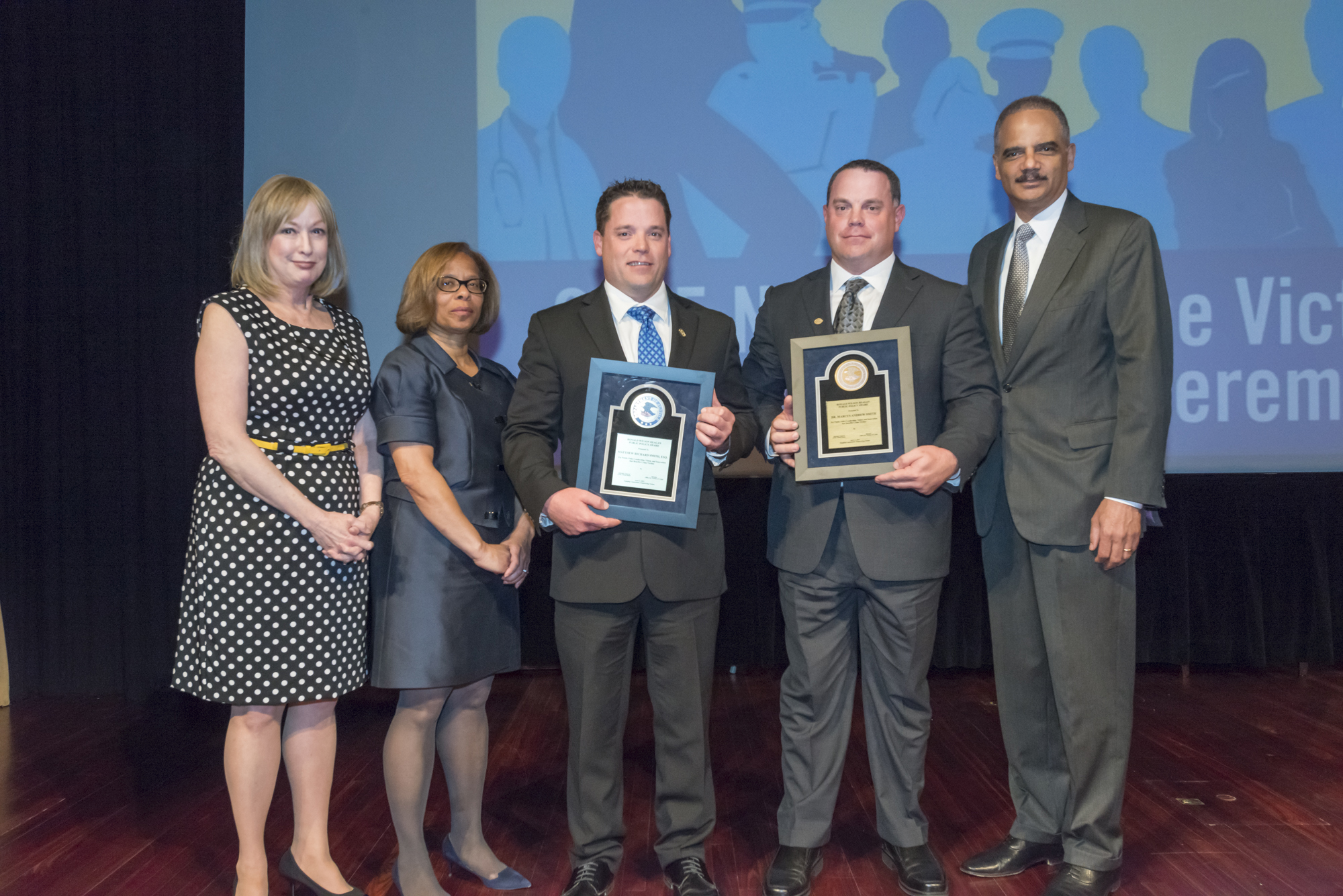 2015 National Crime Victim Service Award recipients Matthew Richard Smith and Dr. Marcus Andrew Smith with (from left) Joye E. Frost, Director, Office for Victims of Crime; Karol V. Mason, Assistant Attorney General, and Attorney General Eric H. Holder, Jr.