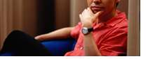 Photo of an Asian man sitting on a couch, resting his chin on his hand.