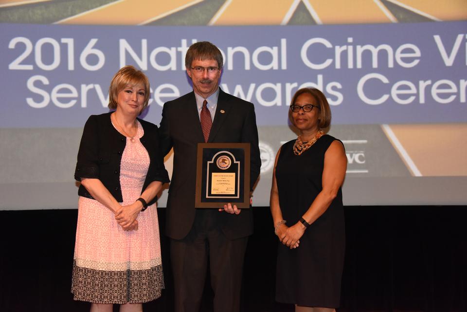 2016 Crime Victims’ Rights Award recipient Russell P. Butler accepts the award with (from left) Joye E. Frost, Director, Office for Victims of Crime and Karol V. Mason, Assistant Attorney General.