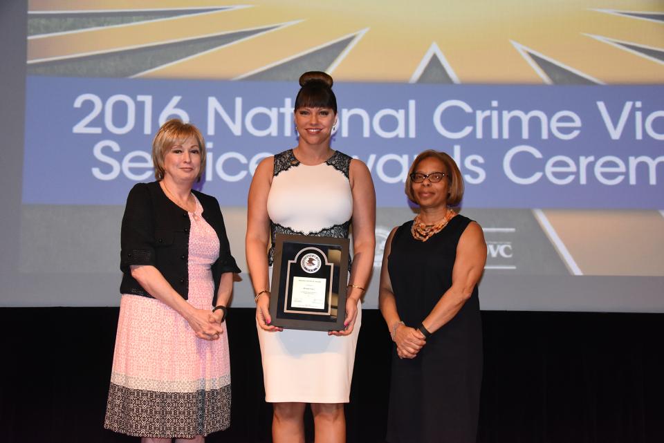 2016 Special Courage Award recipient Brenda Tracy accepts the award with (from left) Joye E. Frost, Director, Office for Victims of Crime and Karol V. Mason, Assistant Attorney General.