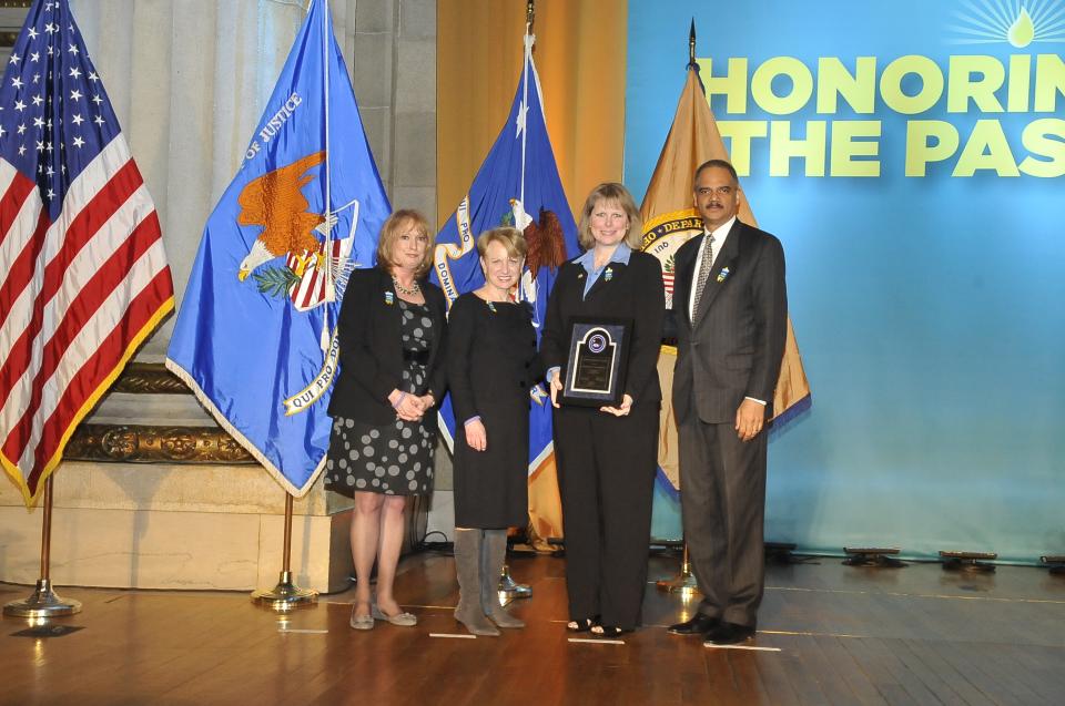 2011 Federal Service Award recipient Charlotte L. Moerbe, Ph.D., stands with (from left) Joye E. Frost, Acting Director, Office for Victims of Crime; Assistant Attorney General Laurie O. Robinson, Office of Justice Programs; and U.S. Attorney General Eric H. Holder, Jr.