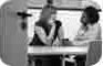 Cropped image of poster featuring two women, viewed through an open doorway, seated at a table and talking. Cropped image of poster featuring two women, viewed through an open doorway, seated at a table and talking.