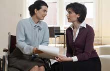 Photo of two seated women, one in a wheelchair, discussing a document one of them is holding.