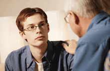 Photo of counseling session; shows an older man placing his hand in support on the younger man�s shoulder.